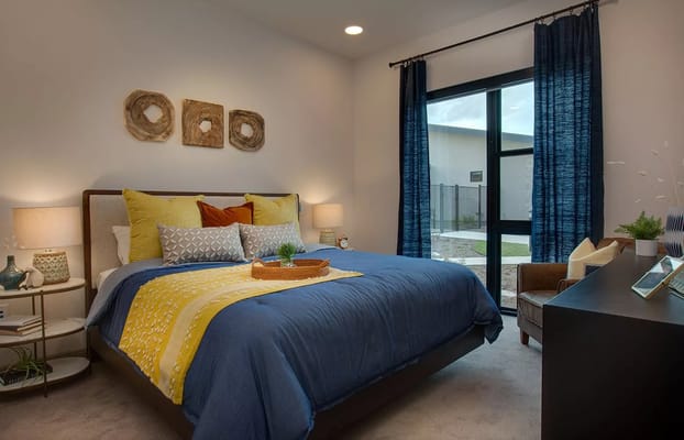 A cozy bedroom with blue and yellow bedding, a basket on the bed, and a window view.