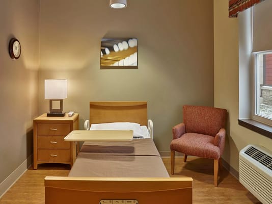 A neatly arranged bedroom featuring a hospital bed, lamp, and cozy chair.