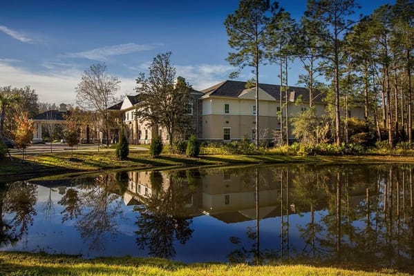 Exterior view of assisted living facility with pond and trees
