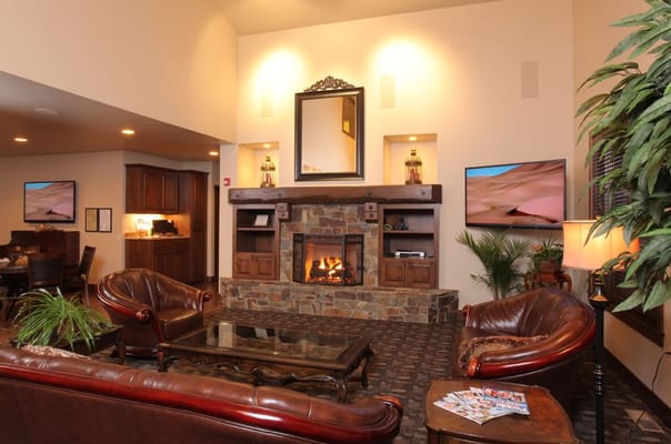 A cozy living room with a stone fireplace, leather chairs, and a large mirror.