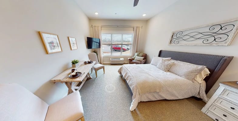 A cozy, well-furnished bedroom with a bed, a wooden table, and a chair overlooking the parking lot.