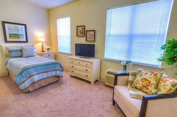 Spacious bedroom with a bed, lamp, TV, and seating area.