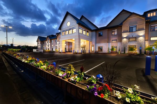 The Moments Memory Care building illuminated at night with flower beds in the foreground.