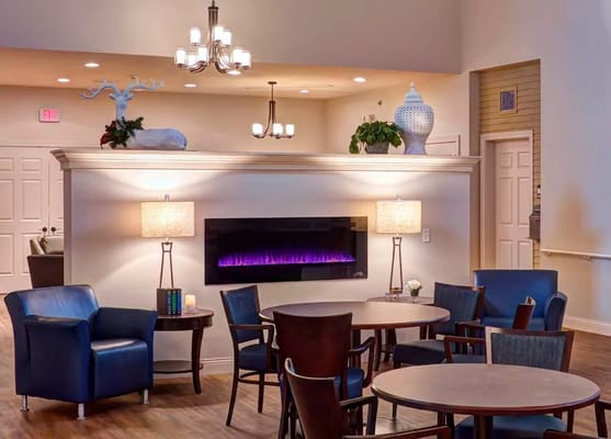 Cozy lounge with blue chairs, tables, and an electric fireplace