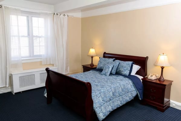 A well-furnished bedroom with a bed, two lamps, and natural light from a window.