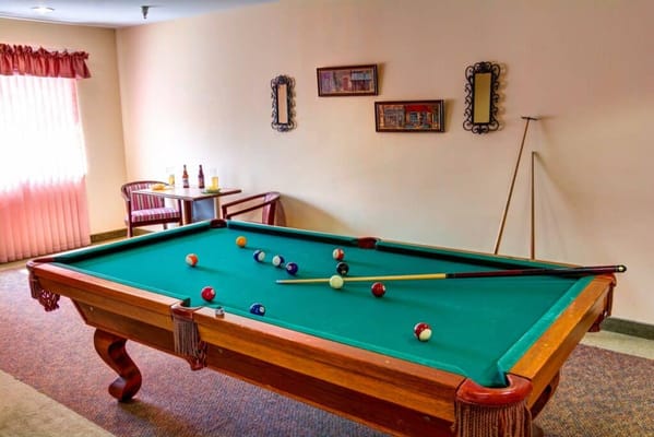 A billiard table with colorful balls and cues in a well-lit game room.