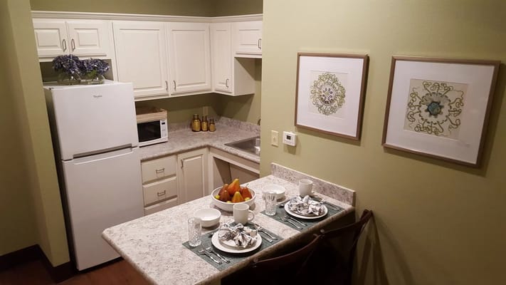 A kitchen with a dining table set for two, featuring fruit and tableware.