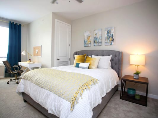 A well-decorated bedroom featuring a gray tufted headboard, vibrant throw pillows, a desk, and a lamp.