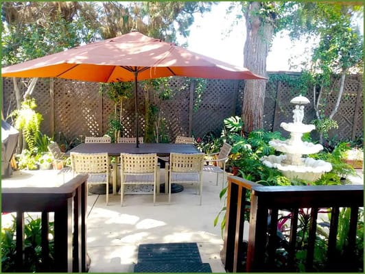 A tranquil garden patio with an umbrella, outdoor seating, and a fountain.