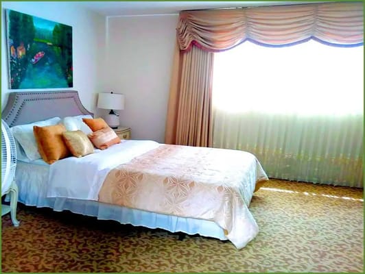 Cozy bedroom with a queen bed, decorative pillows, and large window with curtains.