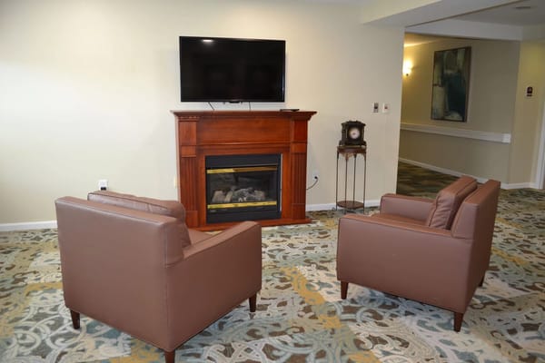 Living room area with two brown chairs and a TV above a fireplace.