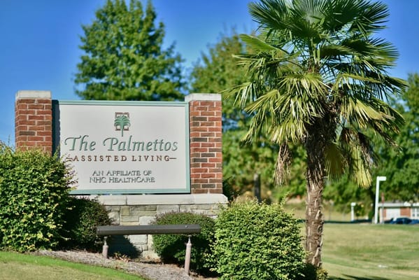 Sign for The Palmettos Assisted Living facility surrounded by greenery.