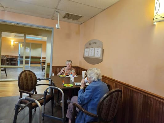 Two senior residents having lunch at a table in The Patriot dining area.