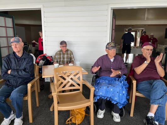 Four senior residents seated in a communal area, with one resident clapping.