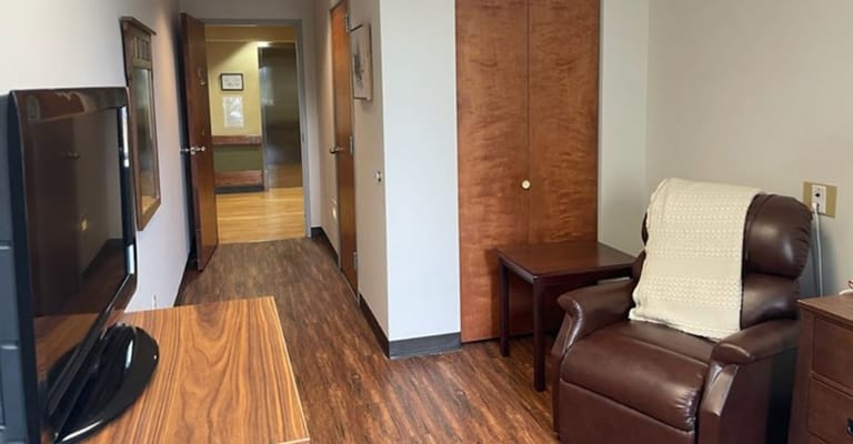 A living room area with a recliner, TV stand, and a door leading to a hallway.