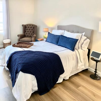 A well-decorated bedroom with a bed, comfortable chair, and warm lighting.