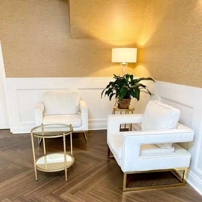 A cozy lounge area with white armchairs, a glass table, and a potted plant.