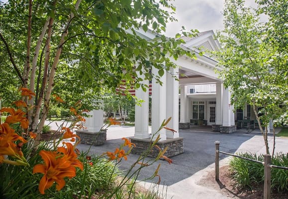 Entrance view of The Residence at Otter Creek, surrounded by greenery and flowers.