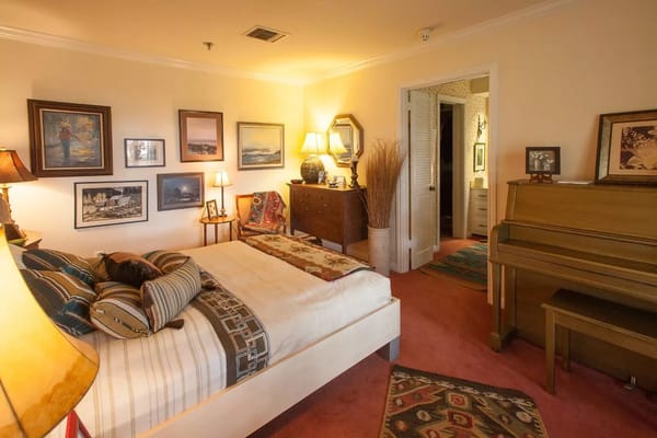 Spacious bedroom with a bed, artwork, and piano.