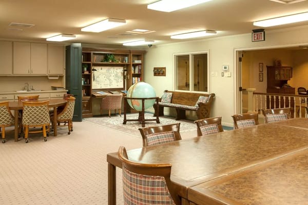 A spacious common area featuring a large wooden table, a globe, and a bookshelf in The Sherick.