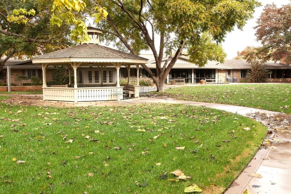 A gazebo surrounded by green grass and trees at The Sherick senior living facility.