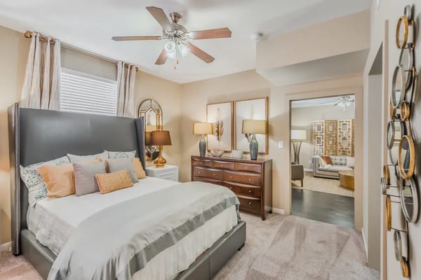 Well-decorated bedroom with grey upholstered bed and wooden dresser.