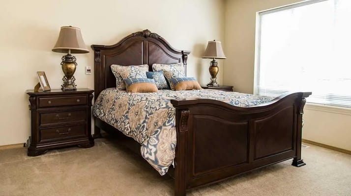 A well-furnished bedroom with a large bed, two bedside lamps, and a window.