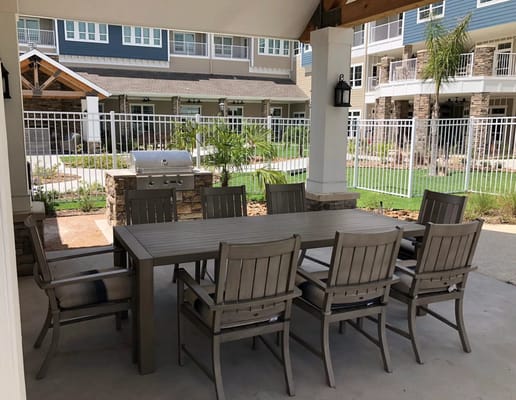 Outdoor dining table with chairs and a grill in a shaded area