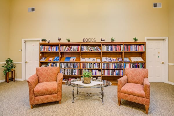 A cozy library lounge with two chairs and a bookshelf filled with books.