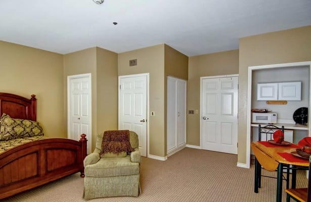 Interior of a cozy room featuring a bed, chair, and kitchenette.