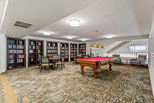 Interior view of the recreational room featuring a billiard table and bookshelves.