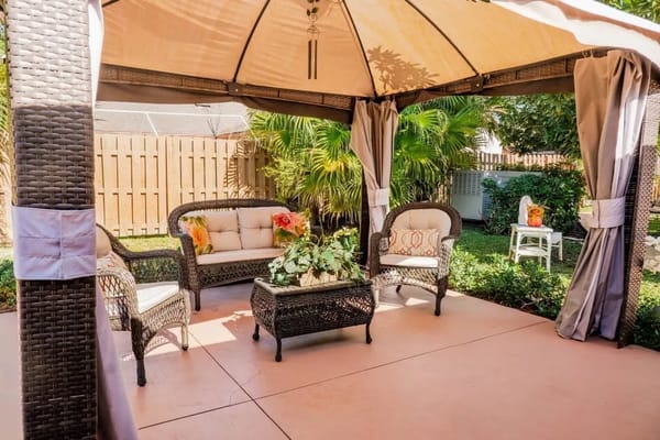 Cozy outdoor seating area with a gazebo, plants, and wicker furniture.