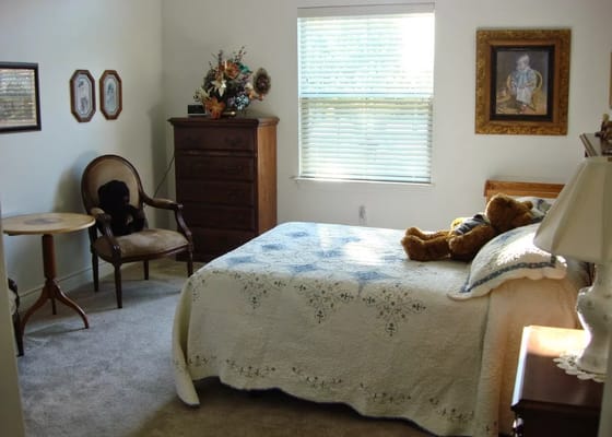 A cozy bedroom with a bed, side table, chair, and chest of drawers