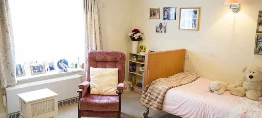 Interior view of a resident's room with a pink bed, chair, and personal decorations.