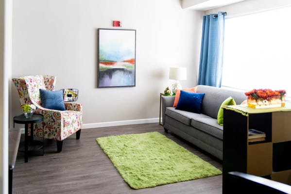 Bright living room with a floral armchair, grey sofa, and colorful decor