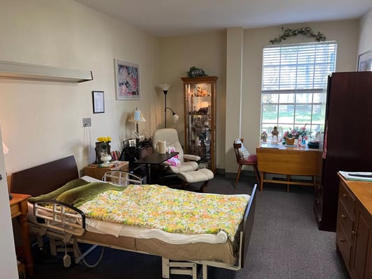 Cozy bedroom in a senior living facility, featuring a hospital bed and seating area.