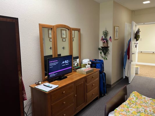 A cozy resident room featuring a dresser, TV, and personal items.