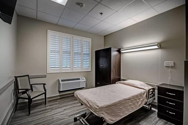 A patient room with a bed, chair, and windows in Trend Health and Rehab of Meridian.