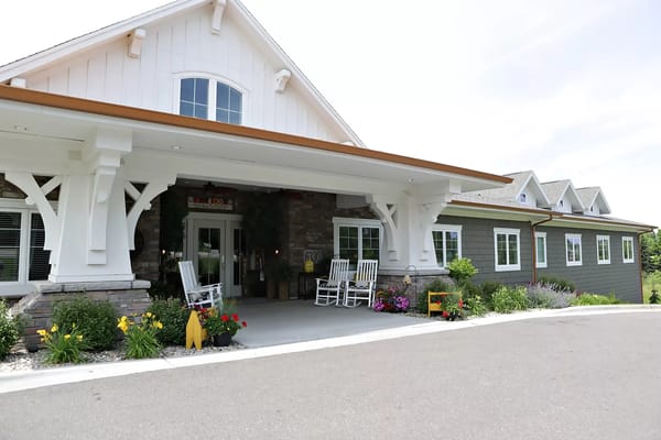 Main entrance of Trouvaille Memory Care Suites with rocking chairs and flowers.