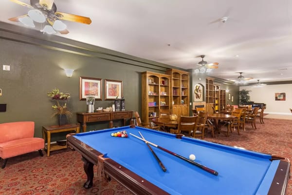 Billiards table with a vibrant blue cloth and various balls, surrounded by seating areas and shelves