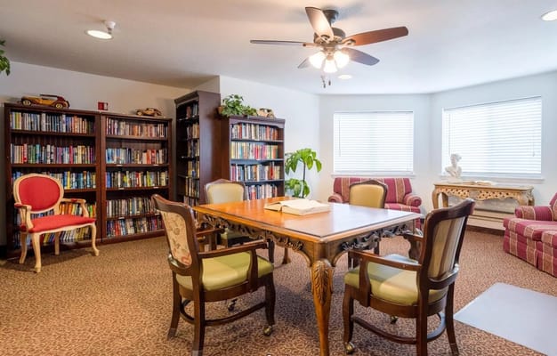 A cozy library with bookshelves, a table, and seating at Ventura Place.