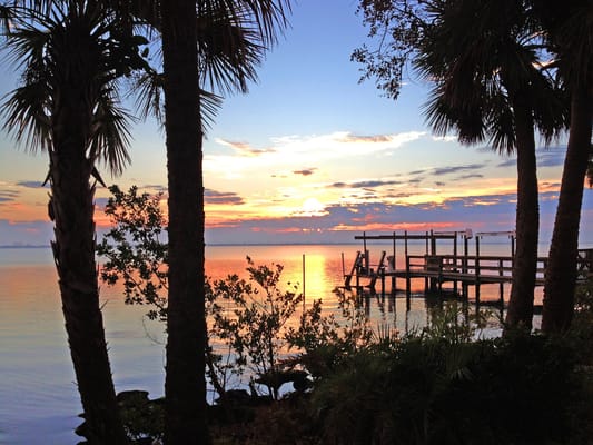Sunset over water with palm trees and a dock
