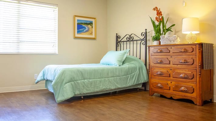 A serene bedroom featuring a bed, dresser, and decorative plants.