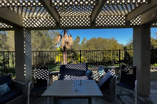 Seating area on the patio with shadow patterns and palm trees in the background.