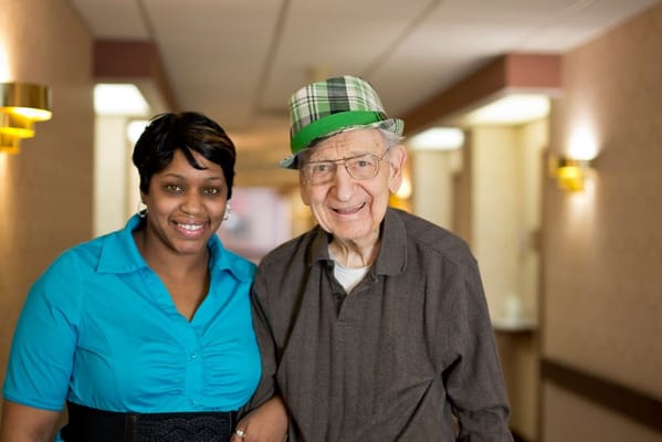Staff member and senior resident smiling together in a hallway