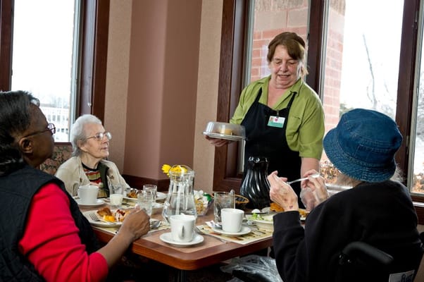 Staff serving food to residents at a dining table.