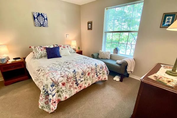 Cozy bedroom featuring a floral bedspread, side tables, and a window with natural light.