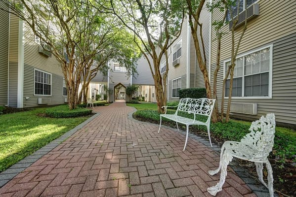A serene courtyard with a paved path and trees, featuring white benches.