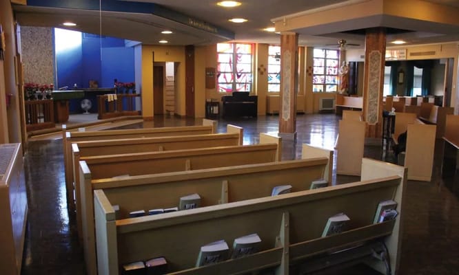 Interior view of the chapel with wooden pews and stained glass windows.