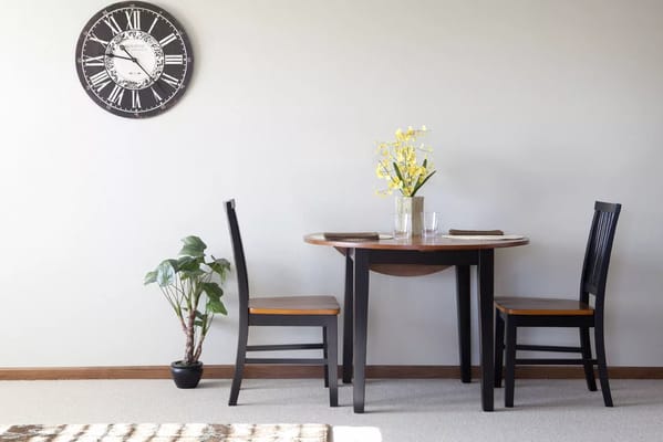 Table setting with two chairs, a plant, and a wall clock